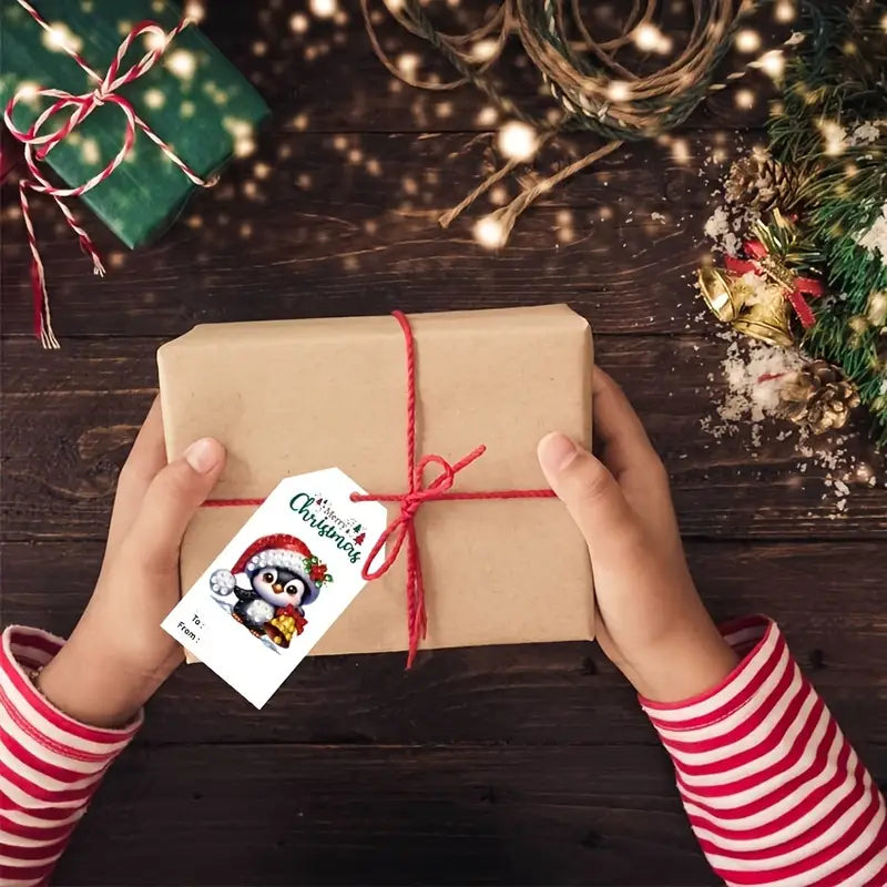 Child's hands holding a wrapped gift with a Christmas tag on a wooden surface with festive decorations.