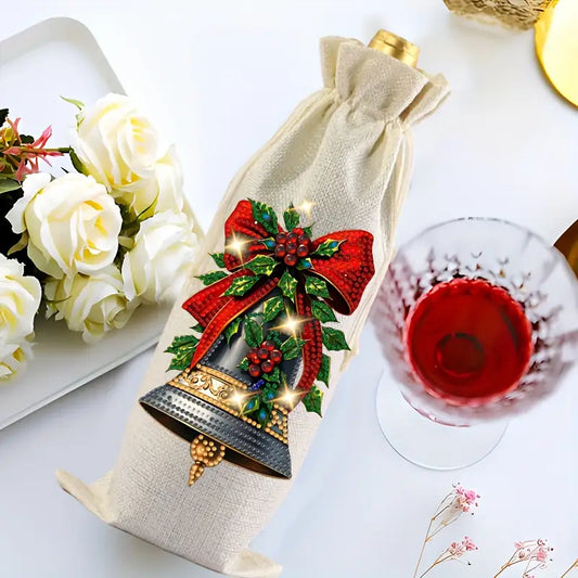 A festive diamond painted linen wine bag featuring a large Christmas bell with a red bow and holly leaves, set next to a wine glass
