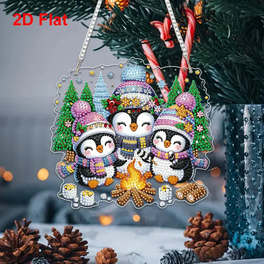 Festive Penguin Campfire Diamond Painting Hanger. A flat acrylic decoration of three penguins in winter hats and scarves sitting around a campfire, decorated with crystal rhinestones