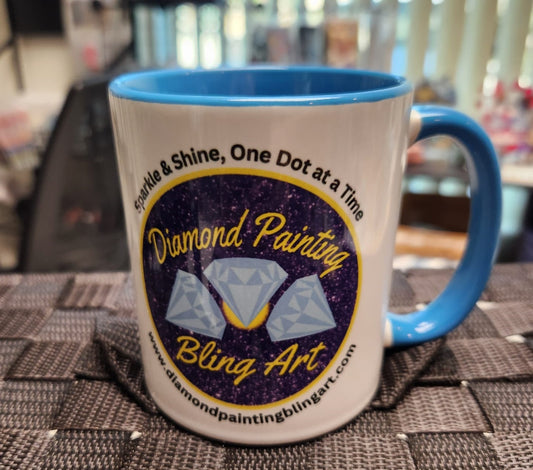 A white ceramic mug with a blue handle and interior, featuring the Diamond Painting Bling Art logo and the tagline "Sparkle & Shine, One Dot at a Time."