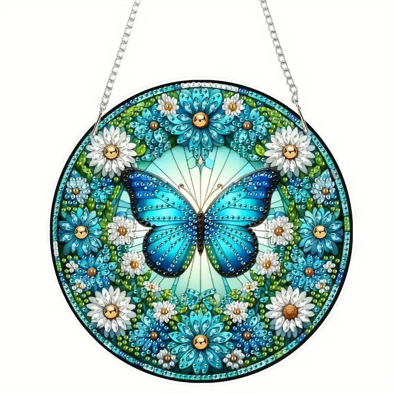 A completed round diamond painting suncatcher featuring a large blue butterfly surrounded by blue and white flowers, hanging from a metal chain.