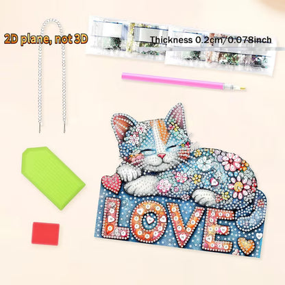 A 2D diamond painting kit for cats, featuring a colorful feline design with the word 'LOVE' and decorative elements, shown with a pink paint pen, green and red sponges, a silver chain, and a strip of rhinestones on a light beige background.