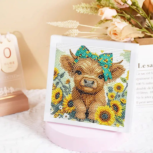A completed mini diamond painting featuring a fluffy highland cow with a blue bow surrounded by bright yellow sunflowers.