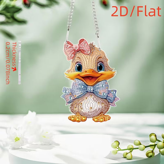 A 2D flat diamond painting pendant shaped like a cute duckling, decorated with pink, blue, and gold rhinestones, hanging from a silver chain against a soft green background with decorative white flowers.