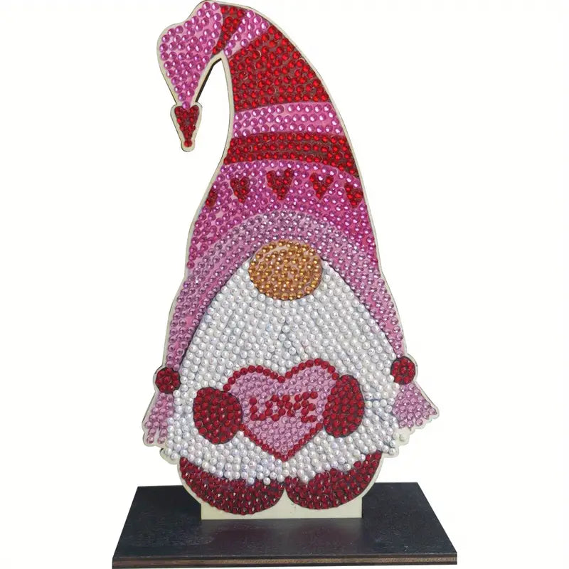A completed diamond painting gnome figure on a dark wooden base, featuring a pink and red hat, white beard, and a heart that says "LOVE."