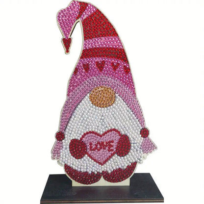 A completed diamond painting gnome figure on a dark wooden base, featuring a pink and red hat, white beard, and a heart that says "LOVE."