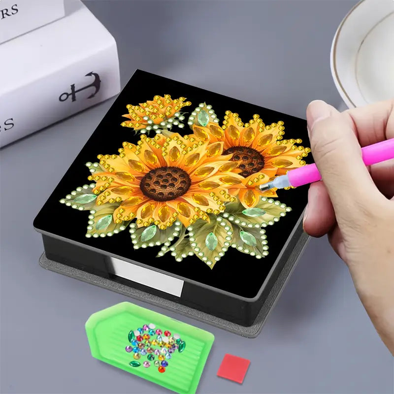 Person using a pink tool to work on a diamond painting project with a sunflower design.